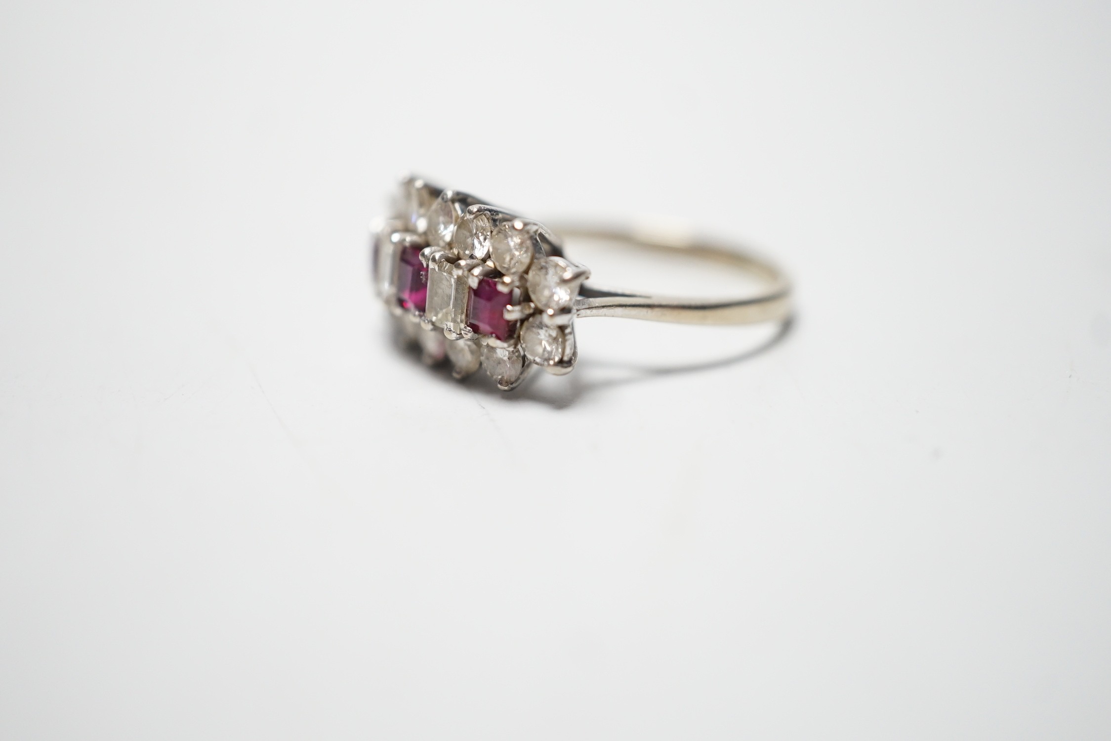 A modern 18ct white gold, square cut ruby and round and baguette cut diamond set cluster ring, size L, gross weight 3.9 grams.